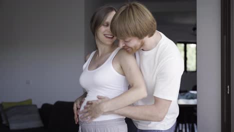 Smiling-husband-walking-and-hugging-his-pregnant-wife
